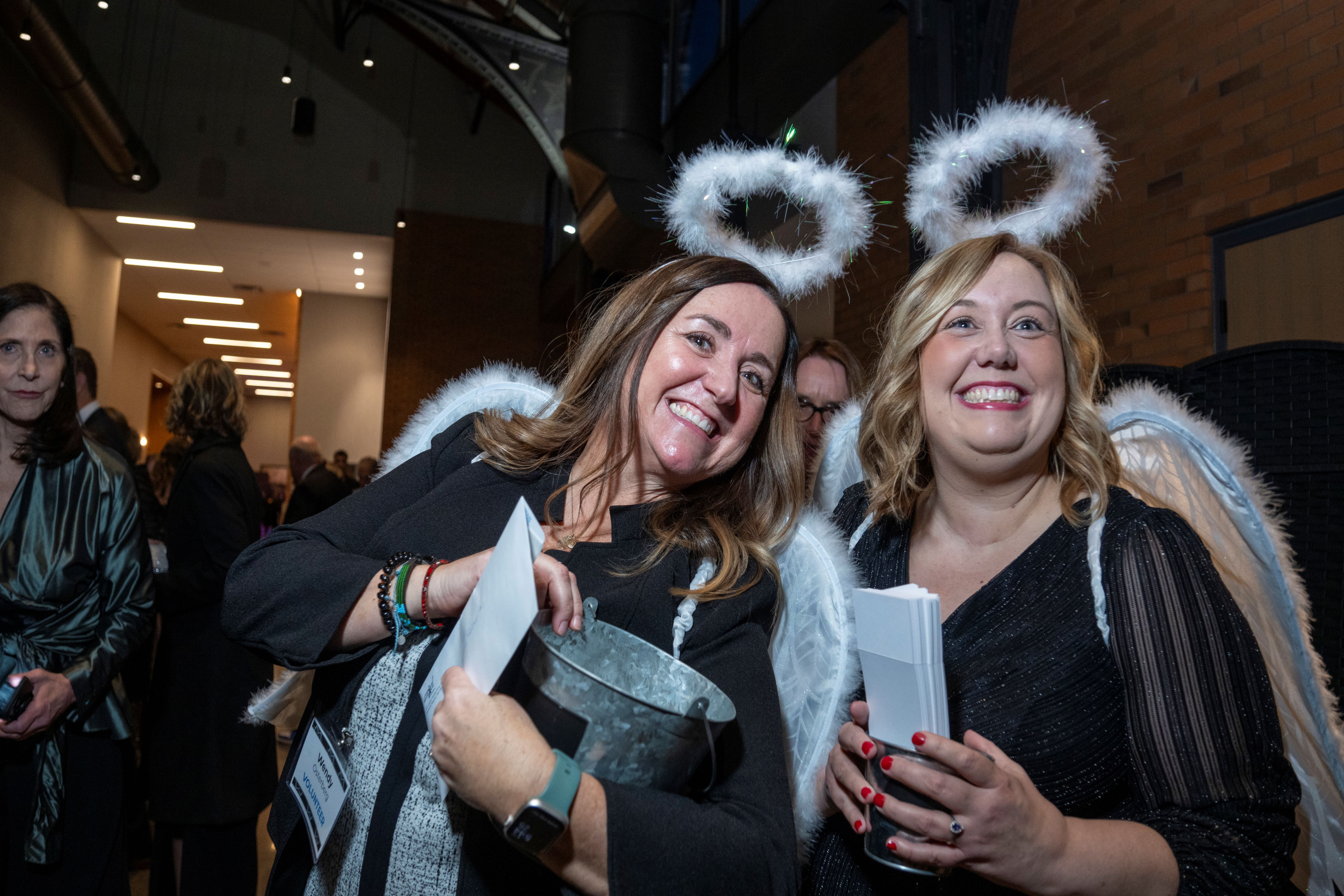 Two women wearing angel wings and halos distribute raffle tickets at the Angel Gala
