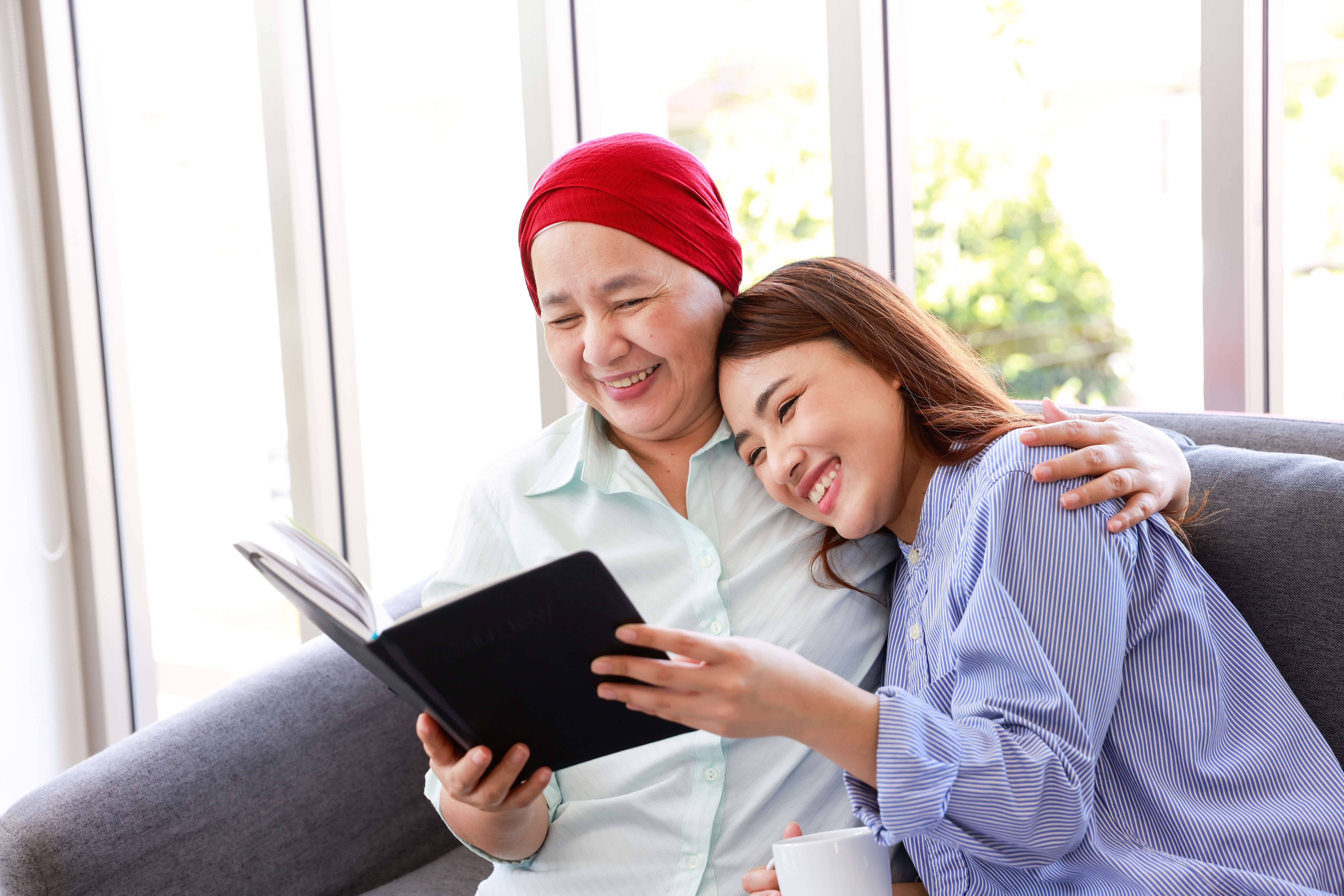 An older Asian woman with cancer and her daughter read about financial literacy.