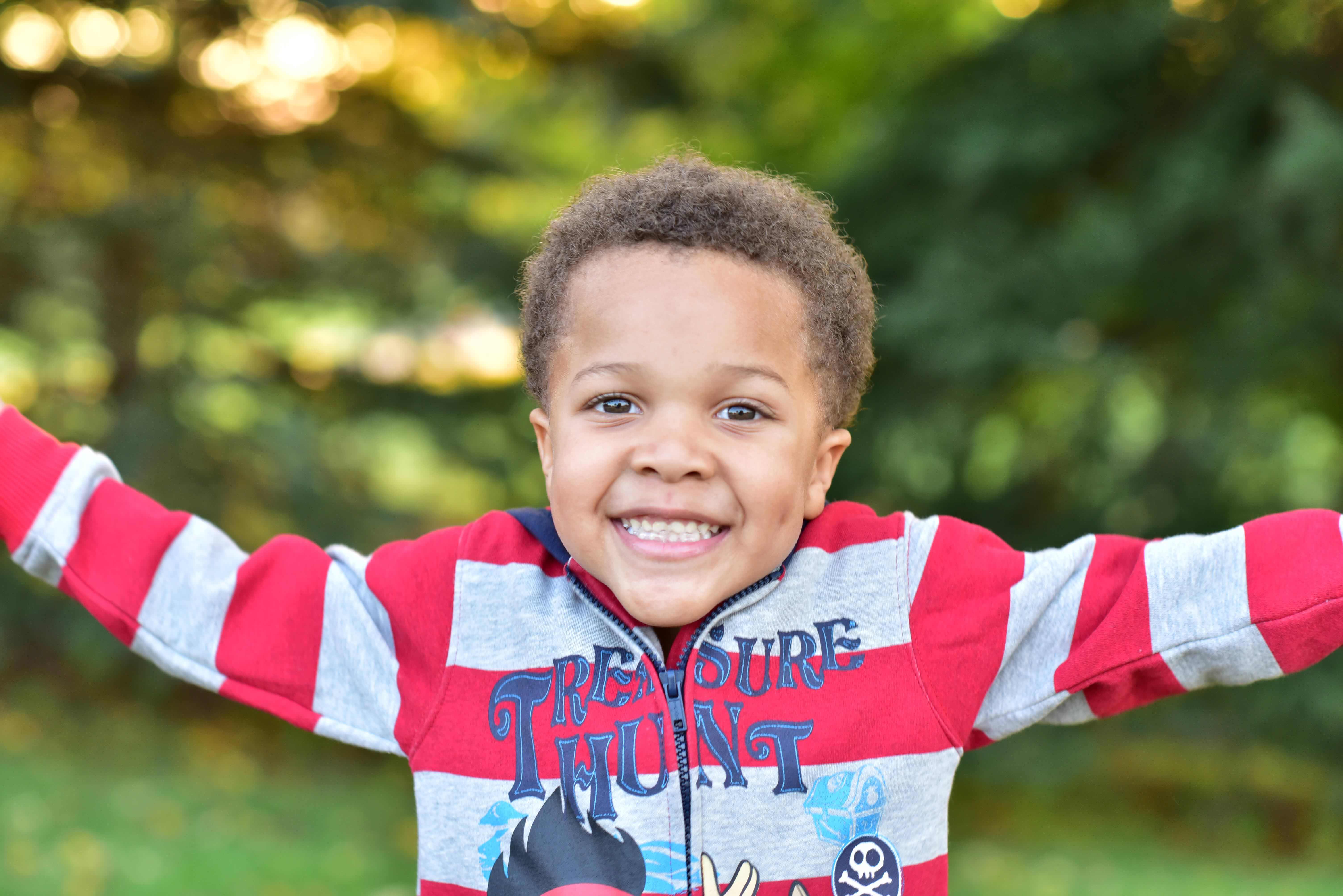 Young African-American boy with a big smile and his arms spread wide.