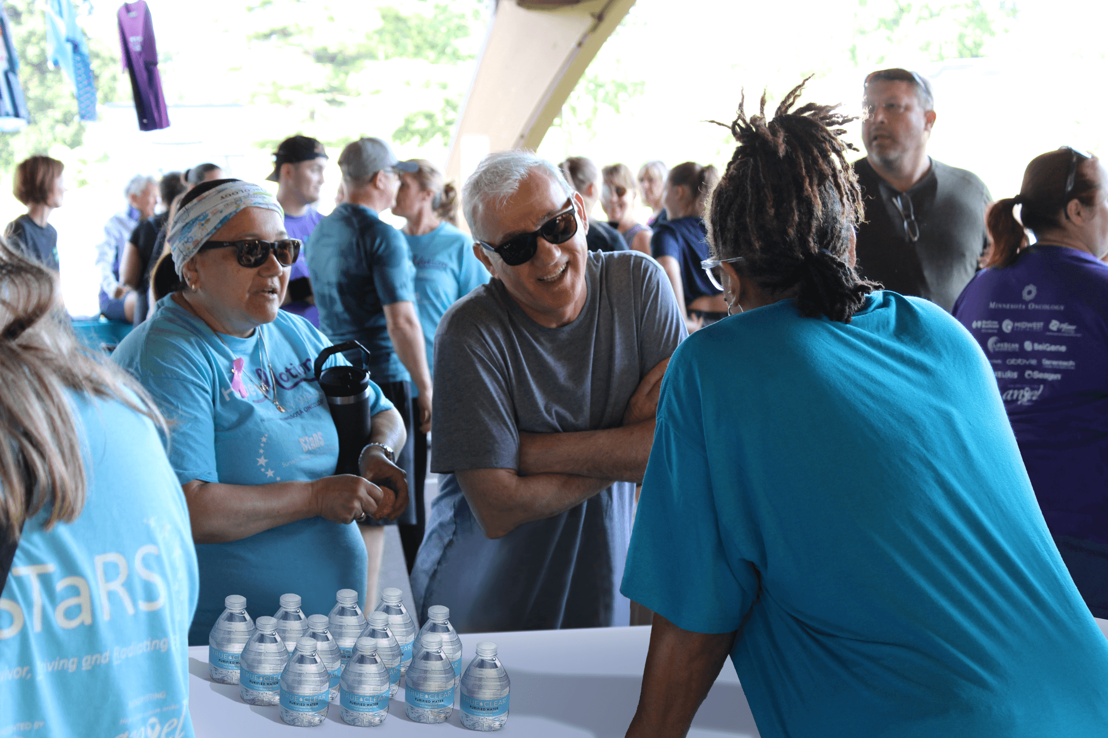 Three individuals talking over a table with a crowd in the background.