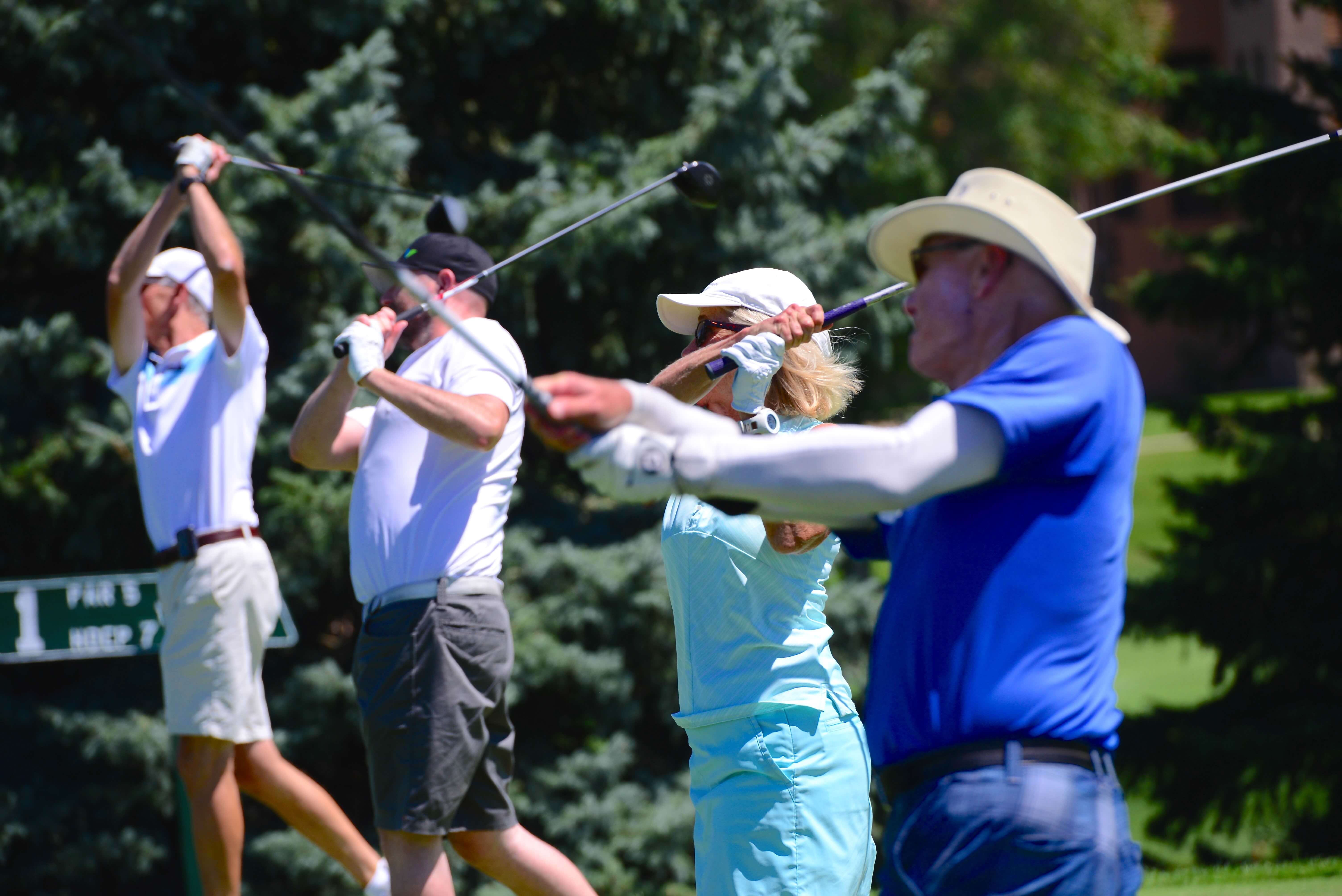 Four golfers swinging their clubs at a golf tournament.
