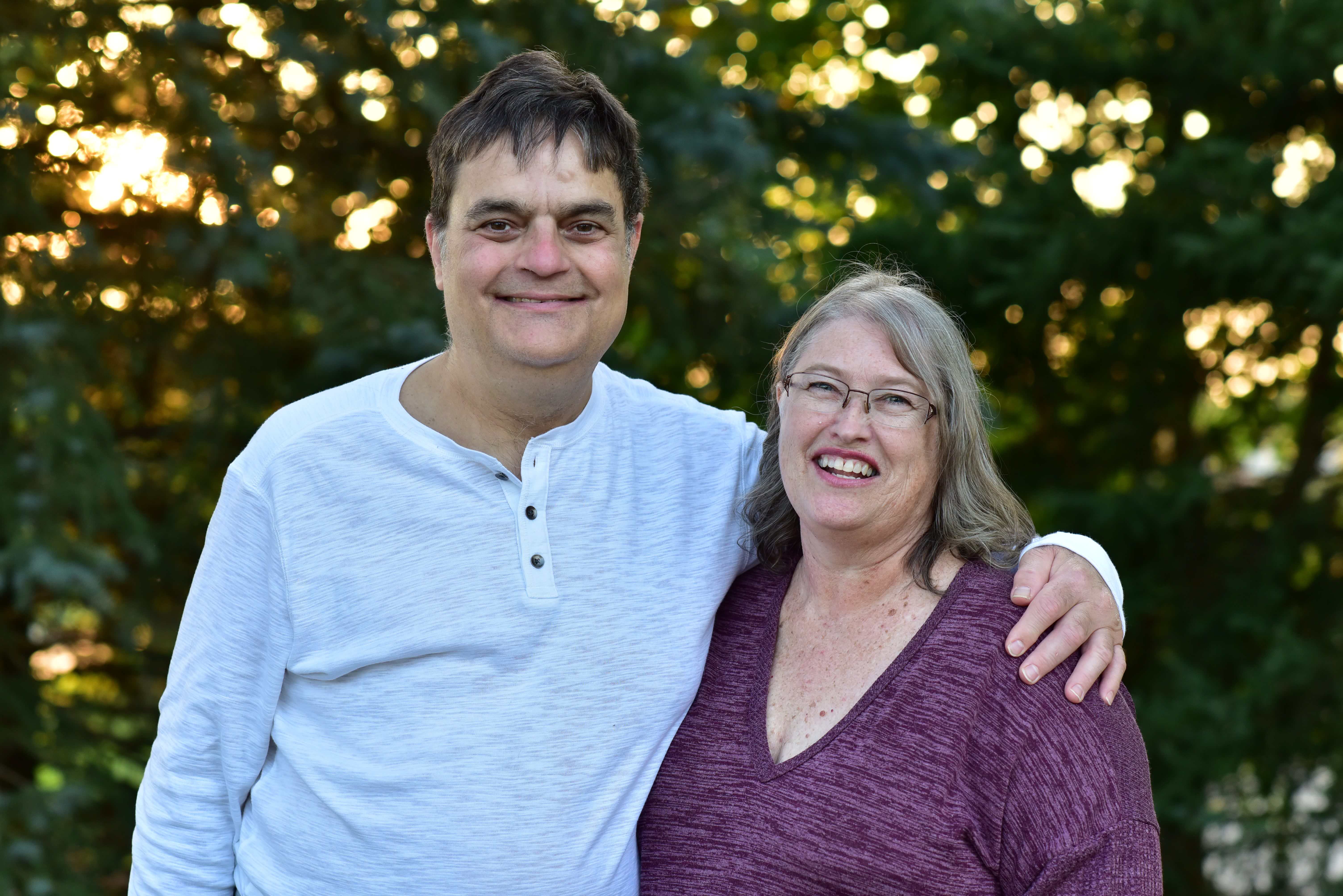 A couple smiles against a leafy background.