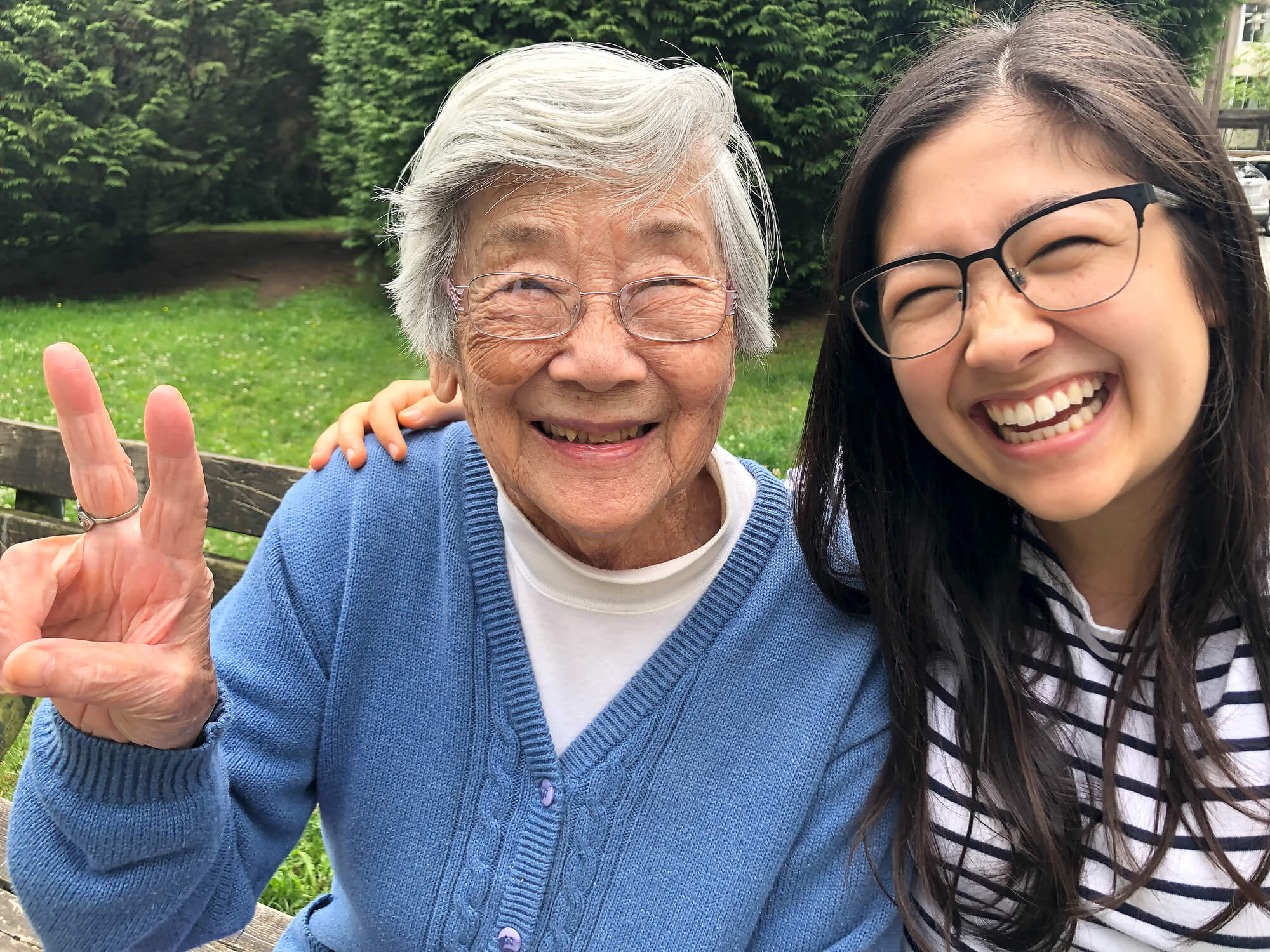 An older Asian woman and a younger Asian woman smiling in a park.