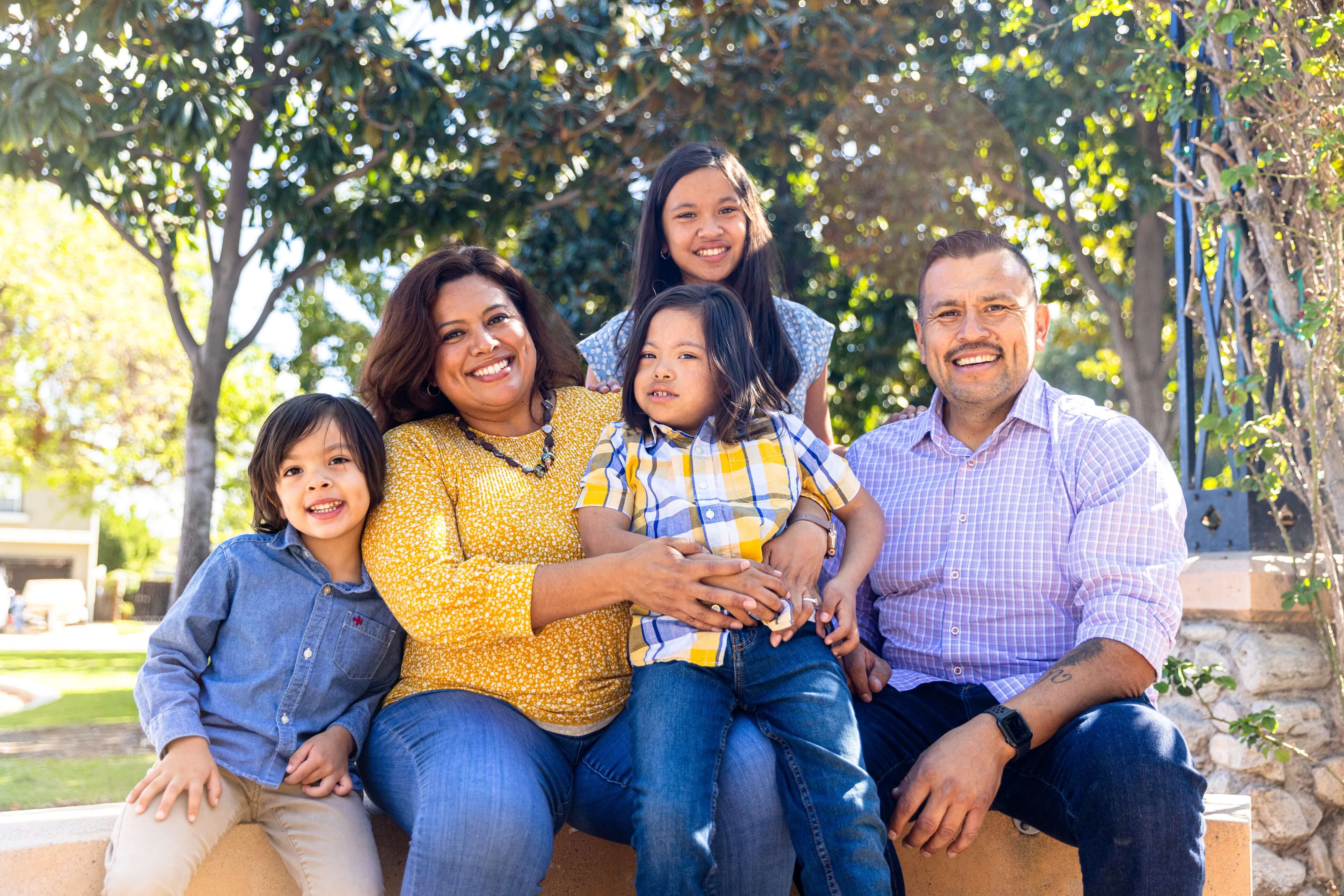 Hispanic family of 5 sitting in a pleasant green space.