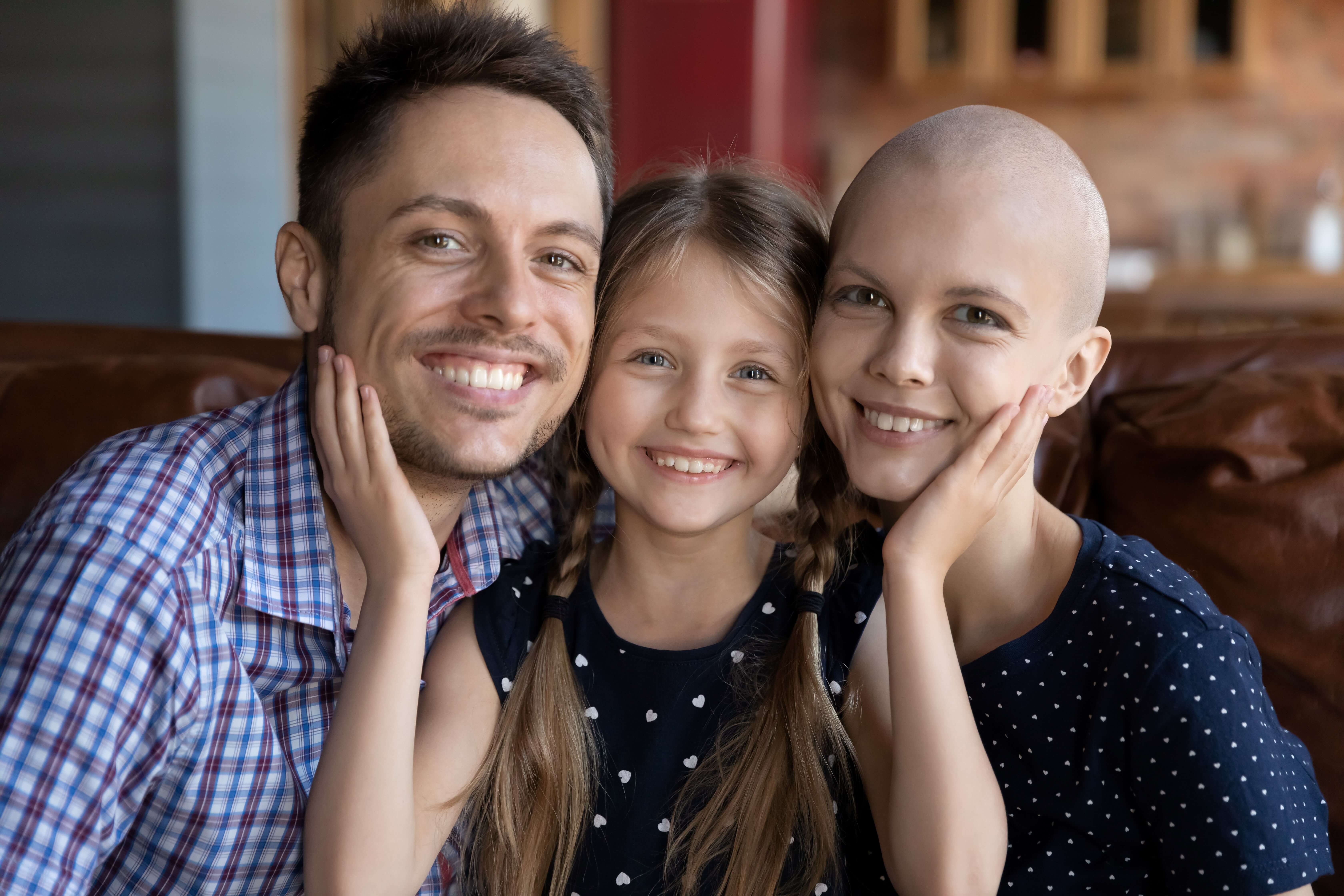 A family of three impacted by cancer smiling.