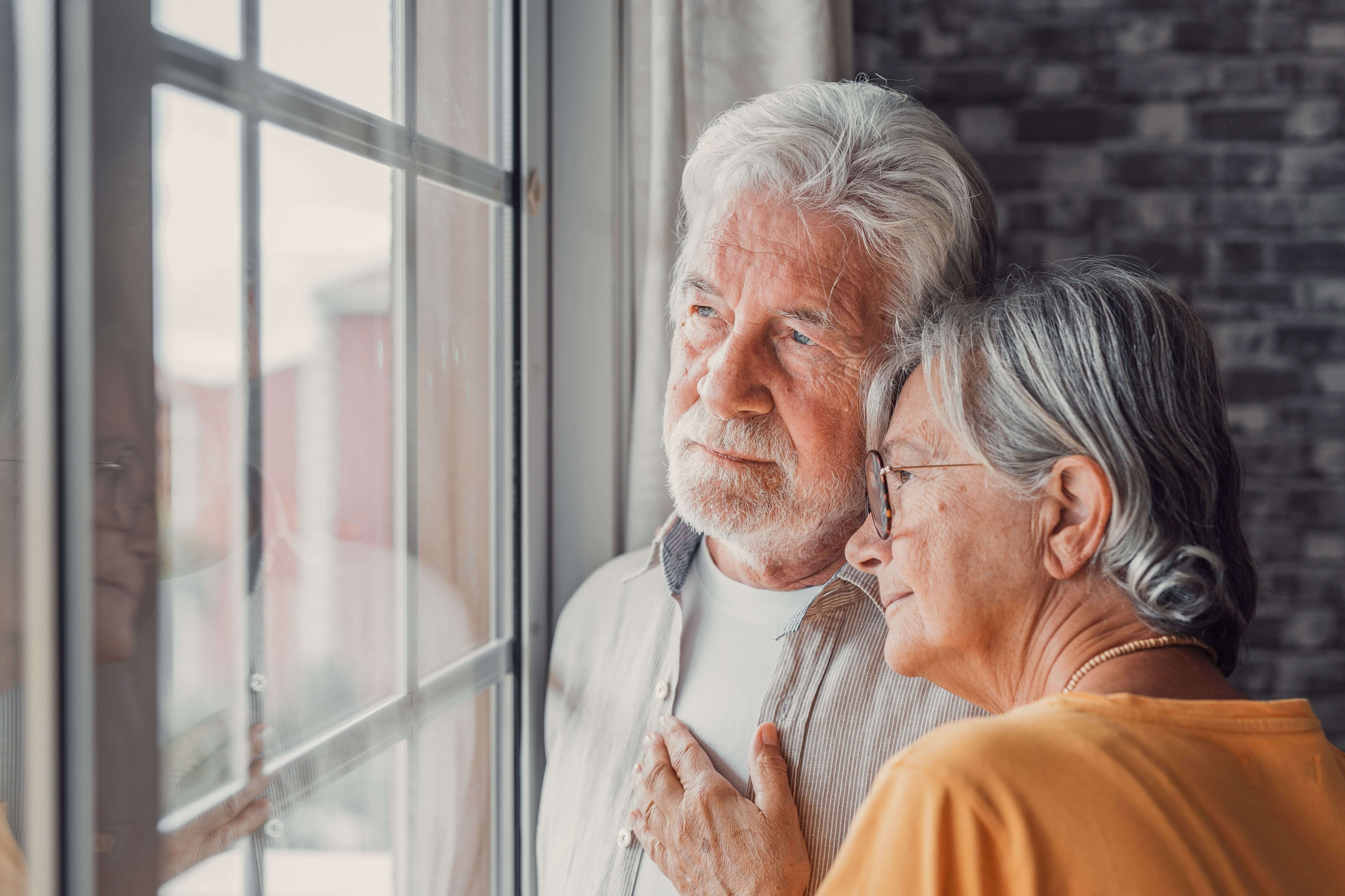 An older couple looking wistfully out a window.