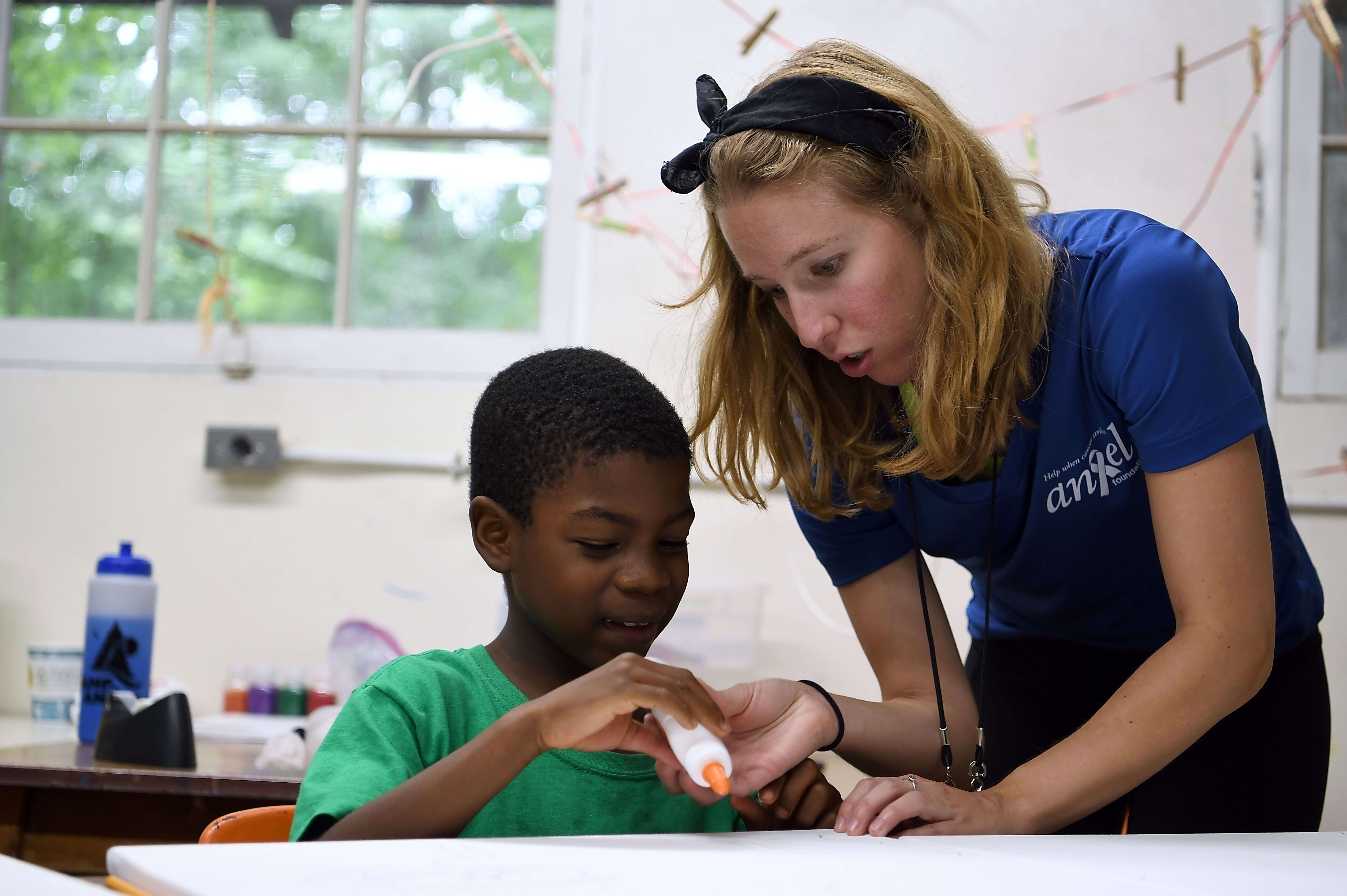 A young woman helps a child with a craft project.