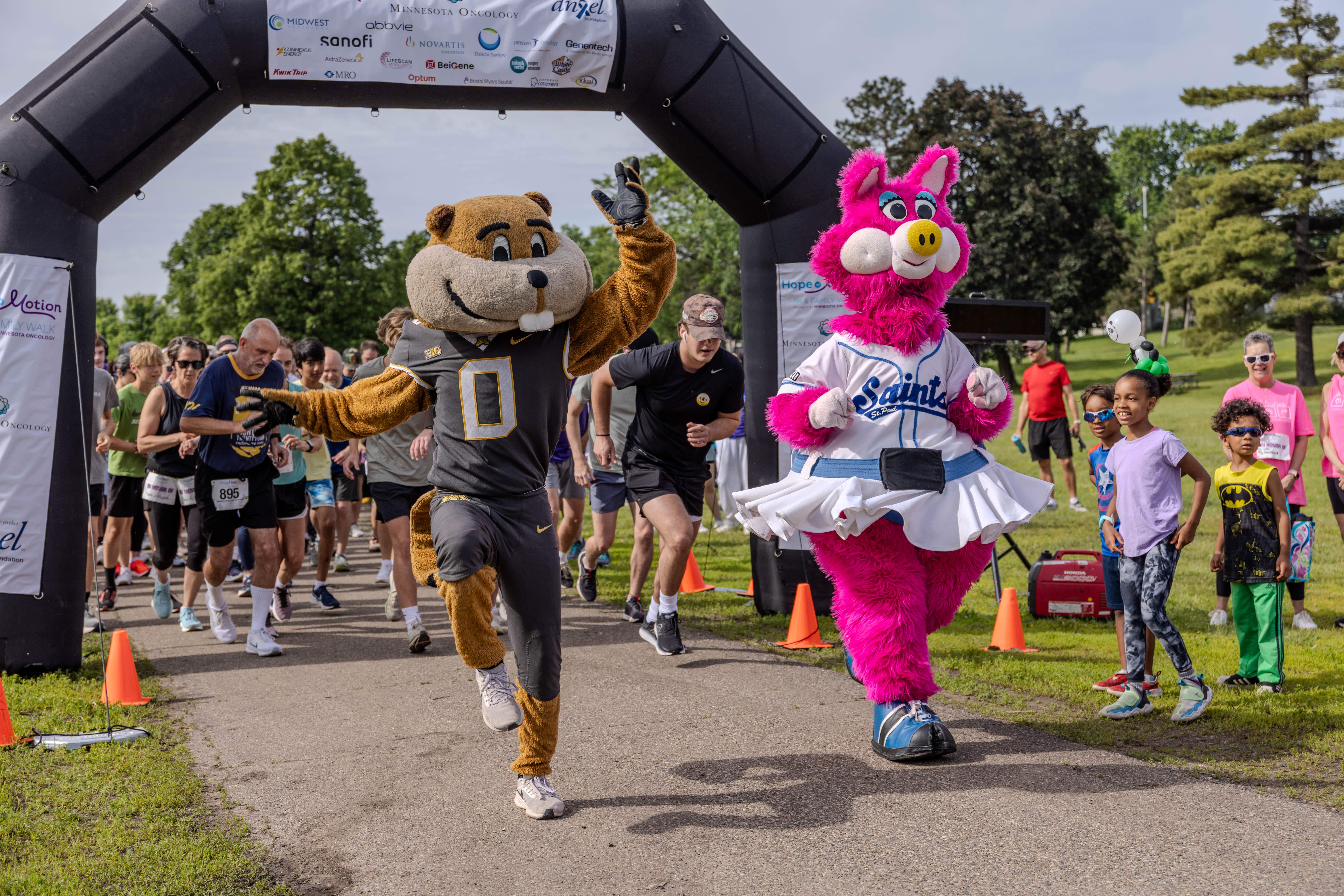 Hope in Motion participants running and walking together, with two mascots leading the group. T-shirts smiling